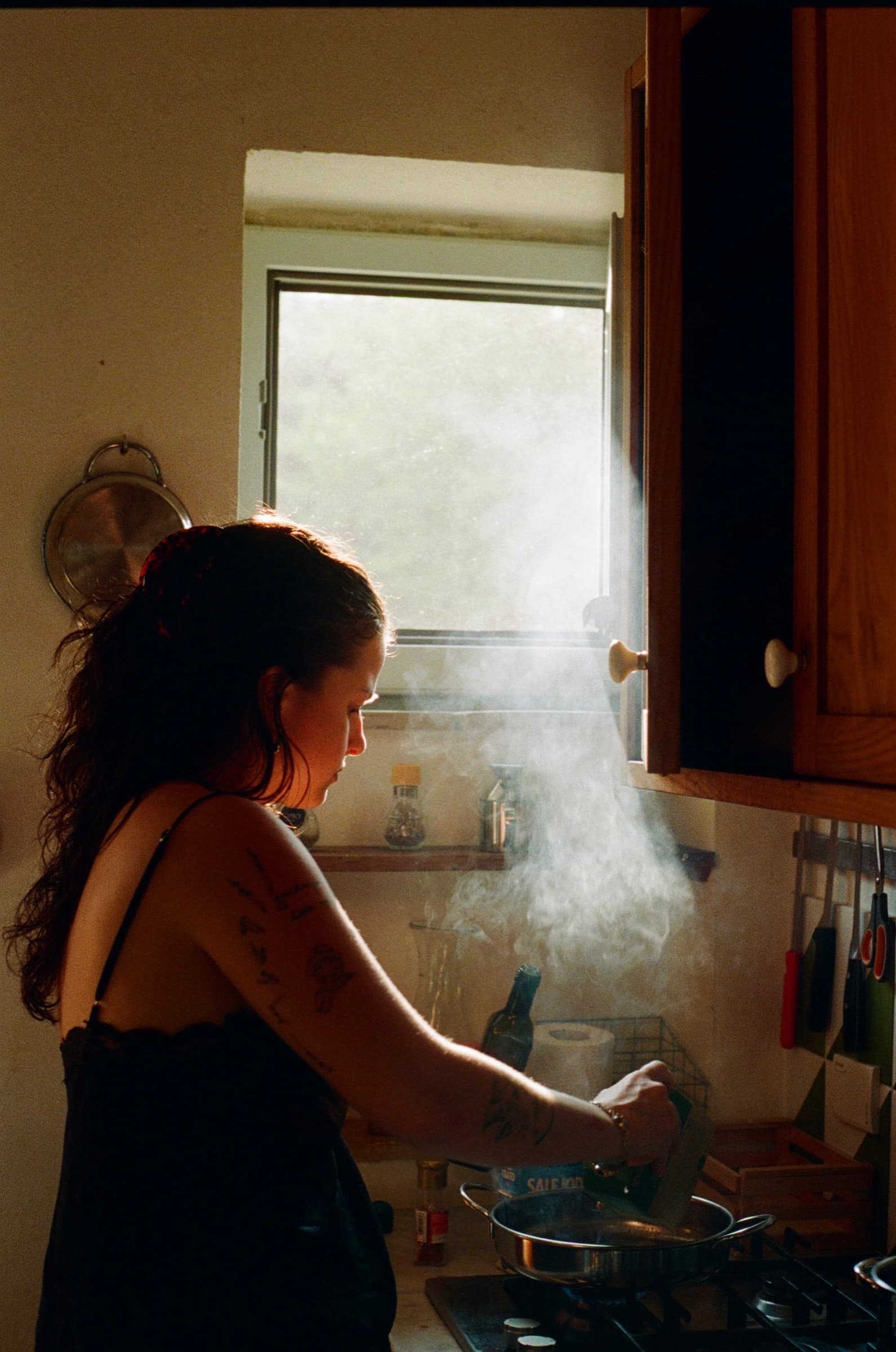 A cook stirring a pan in a sunlit kitchen